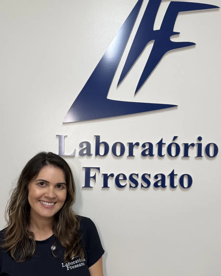 Colaboradora do Laboratório Fressato ao lado da marca na parede da recepção